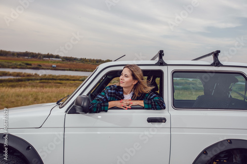 A young woman looks out of the window of an SUV and admires the nature.