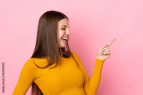 Young caucasian woman isolated on pink background pointing finger to the side and presenting a product