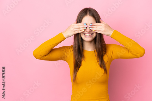 Young caucasian woman isolated on pink background covering eyes by hands and smiling © luismolinero