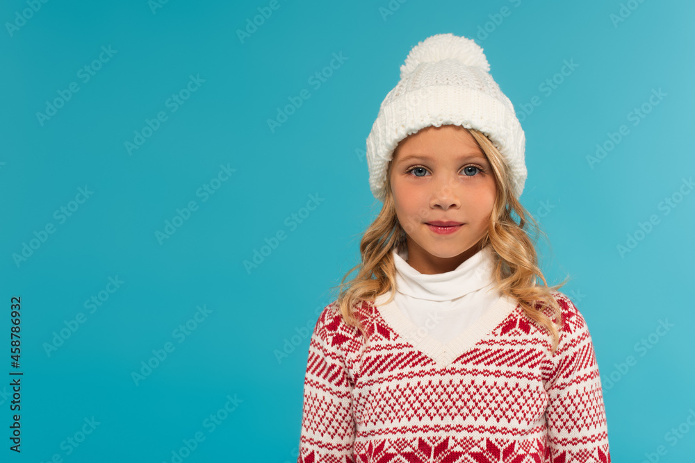 child in knitted hat and warm sweater with ornament looking at camera on blue, new year concept child in knitted hat and warm sweater with ornament looking at camera on blue, new year concept