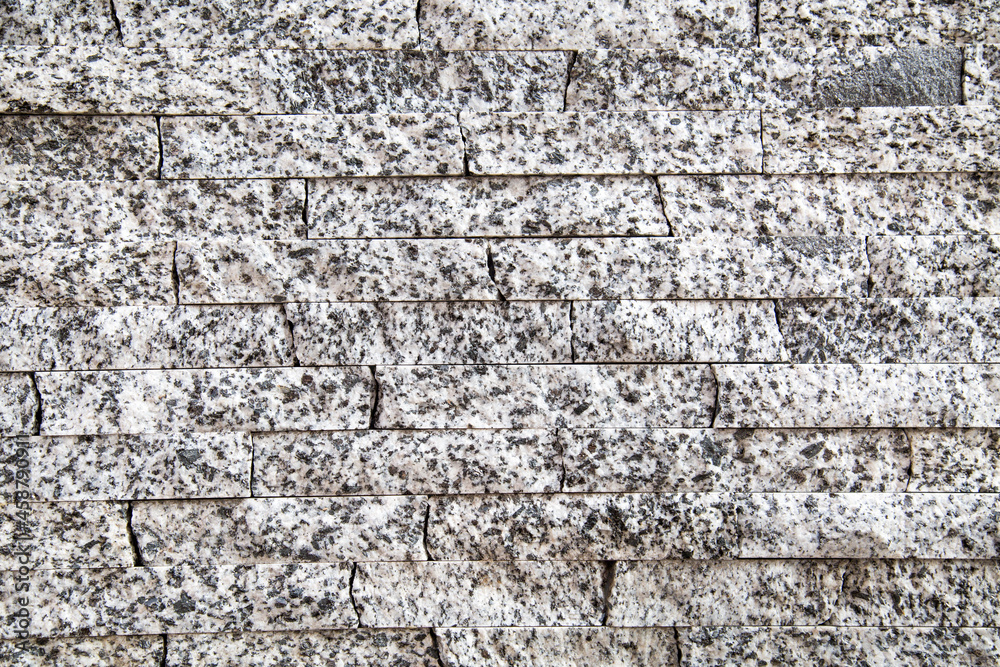 Obraz premium The background of the wall is made of natural granite strips of gray color with black inclusions. Backgrounds texture design.