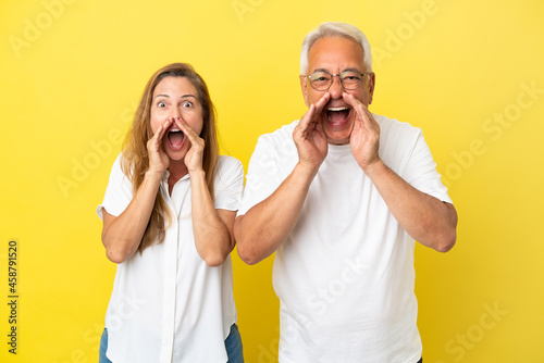 Middle age couple isolated on yellow background shouting with mouth wide open