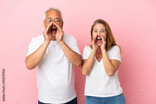 Middle age couple isolated on pink background shouting and announcing something