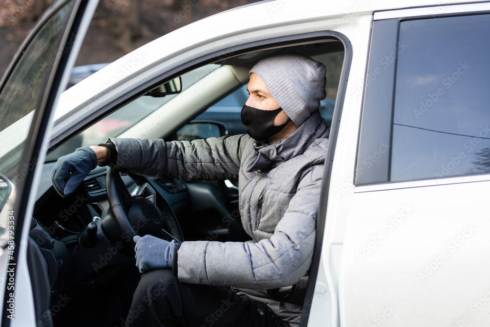 Horizontal shot of man wears spectacles and protective medical face mask, stands near car, commutes to work by personal transport during quarantine. Travel and pandemic situation. Covid-19 concept.