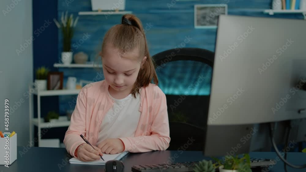 Portrait of child doing homework on notebook for education at desk with computer. Little girl using pen, preparing for remote online class lesson at home. Pupil learning for knowledge Portrait of child doing homework on notebook for education at desk with computer. Little girl using pen, preparing for remote online class lesson at home. Pupil learning for knowledge