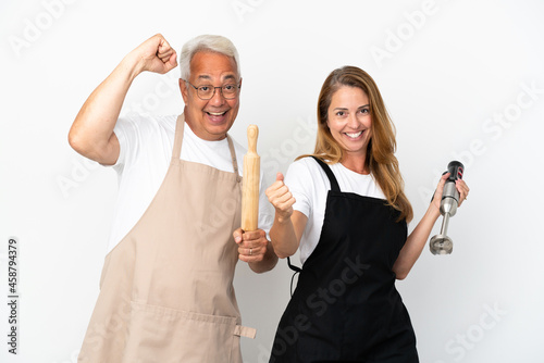 Middle age chefs couple isolated on white background celebrating a victory in winner position