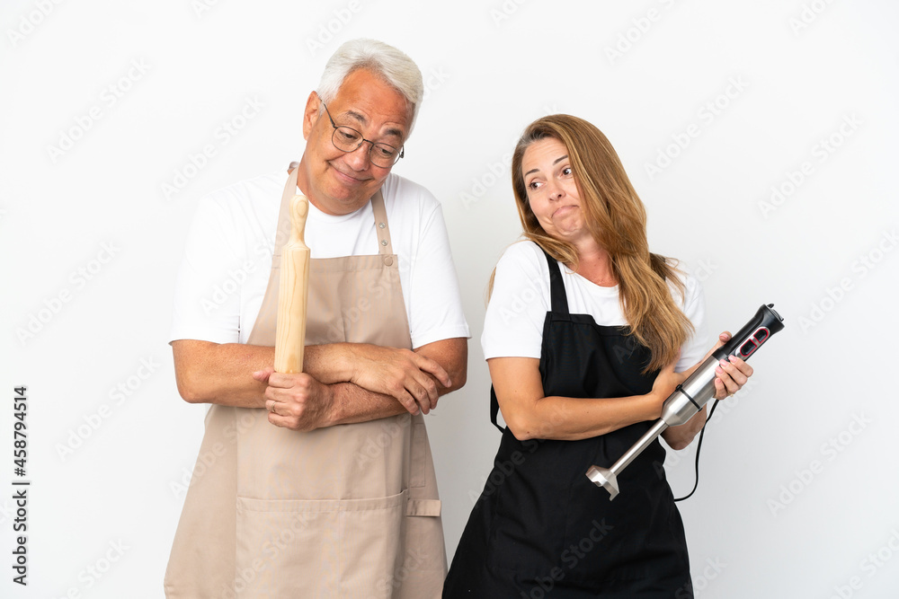 Middle age chefs couple isolated on white background making doubts gesture while lifting the shoulders Middle age chefs couple isolated on white background making doubts gesture while lifting the shoulders