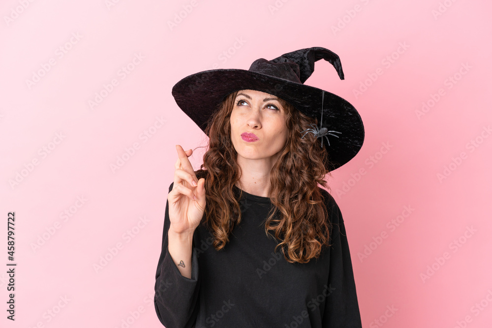 Young caucasian woman celebrating halloween isolated on pink background with fingers crossing and wishing the best