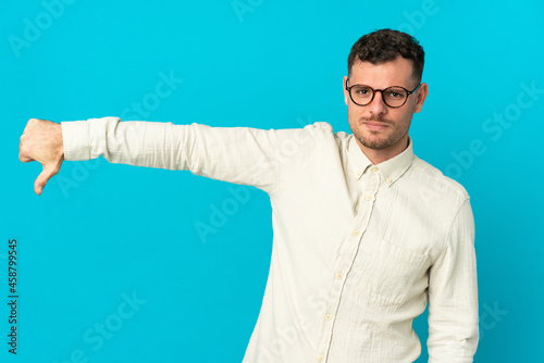 Young caucasian handsome man isolated on blue background showing thumb down with negative expression © luismolinero