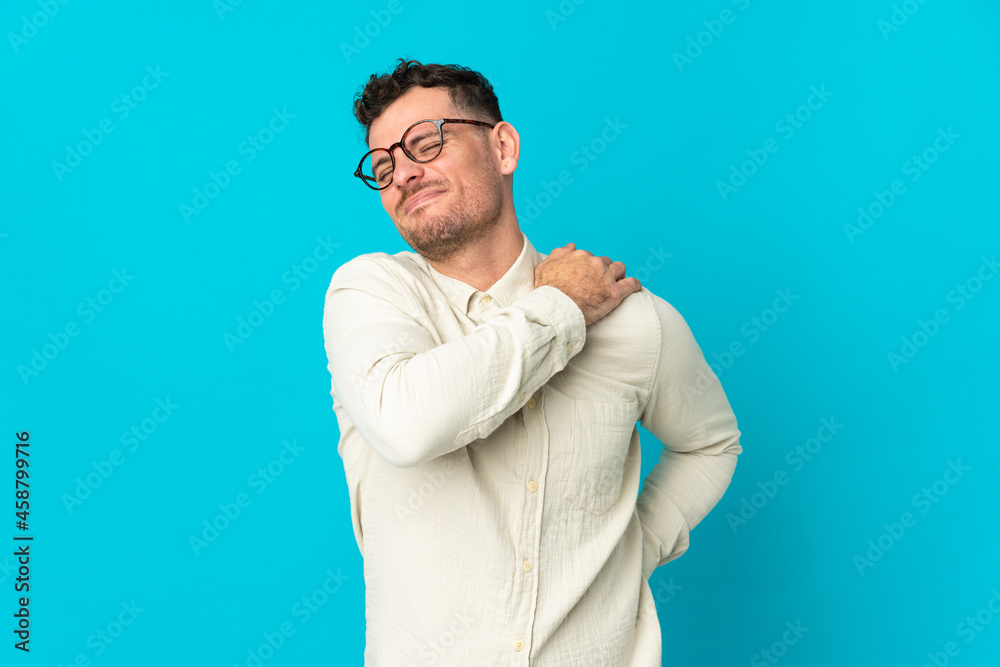 Young caucasian handsome man isolated on blue background suffering from pain in shoulder for having made an effort
