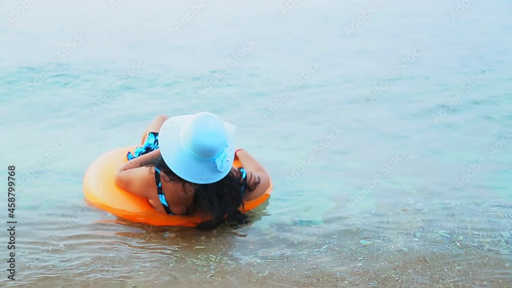 A brunette woman in a blue hat floats in a circle in the sea and looks into the distance