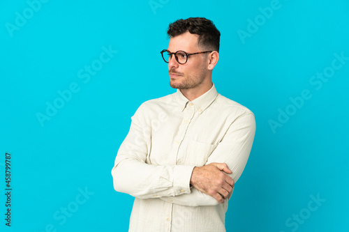 Young caucasian handsome man isolated on blue background keeping the arms crossed