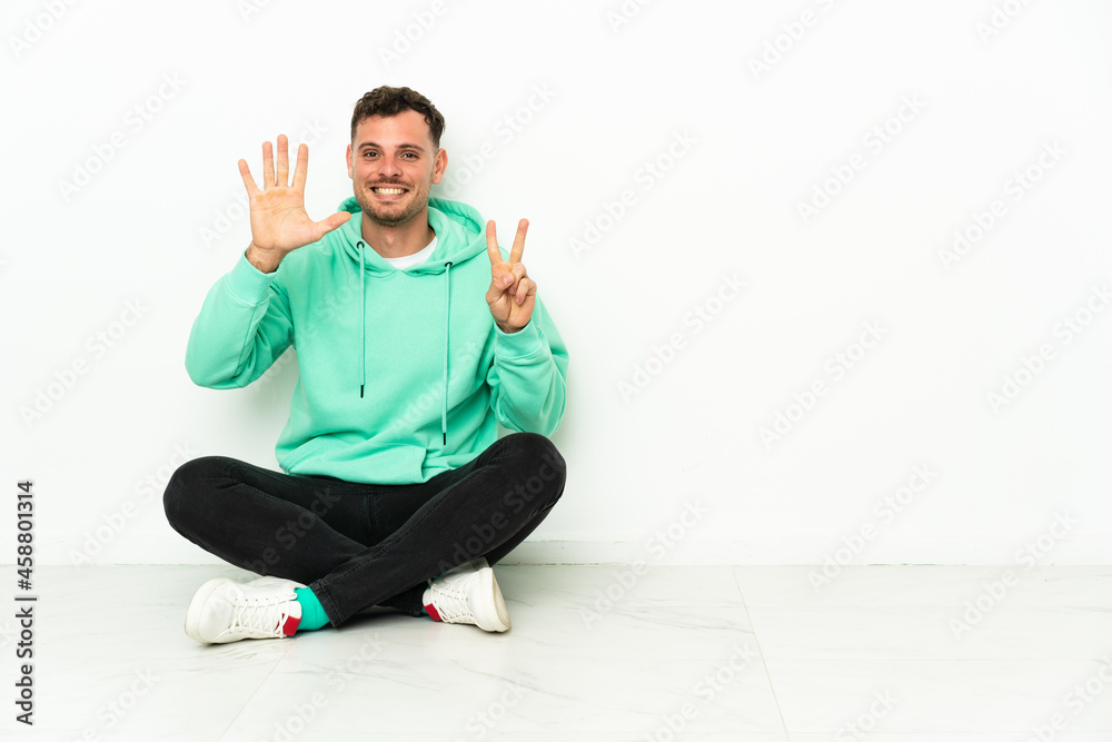 Young handsome caucasian man sitting on the floor counting seven with fingers Young handsome caucasian man sitting on the floor counting seven with fingers