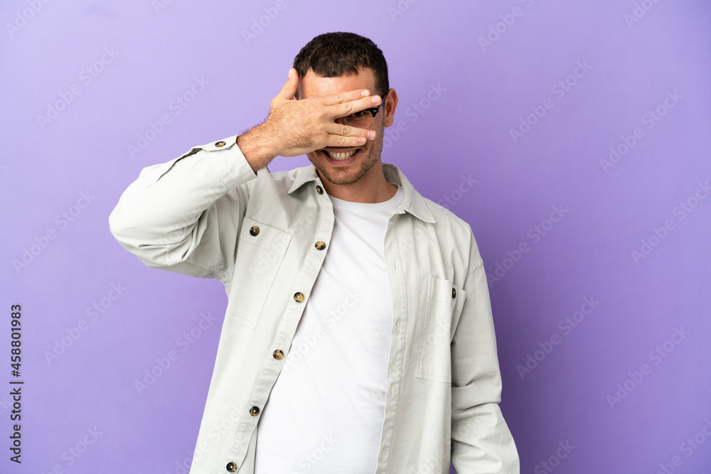 Fototapeta premium Brazilian man over isolated purple background covering eyes by hands and smiling