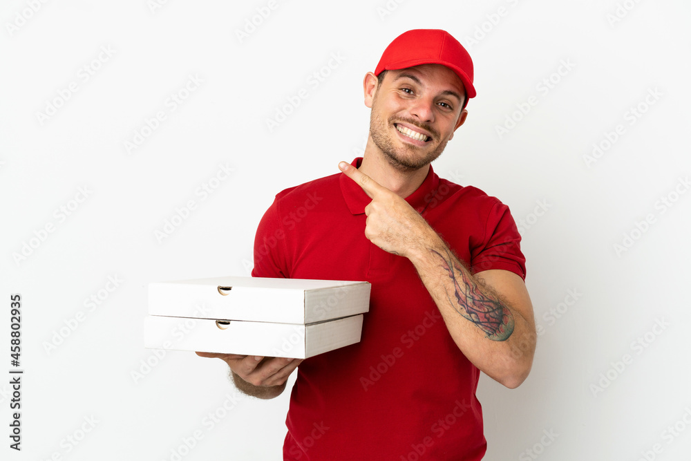 pizza delivery man with work uniform picking up pizza boxes over isolated white wall pointing to the side to present a product pizza delivery man with work uniform picking up pizza boxes over isolated white wall pointing to the side to present a product
