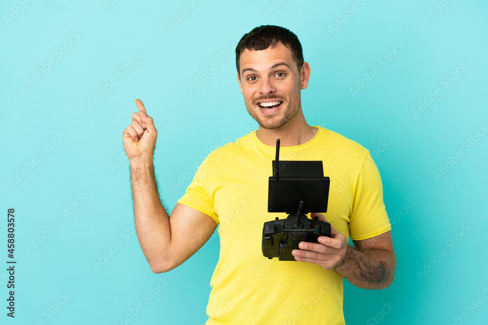 Brazilian man holding a drone remote control over isolated blue background pointing back Brazilian man holding a drone remote control over isolated blue background pointing back