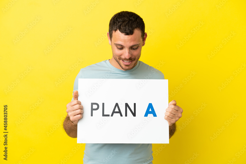 Brazilian man over isolated purple background holding a placard with the message PLAN A Brazilian man over isolated purple background holding a placard with the message PLAN A
