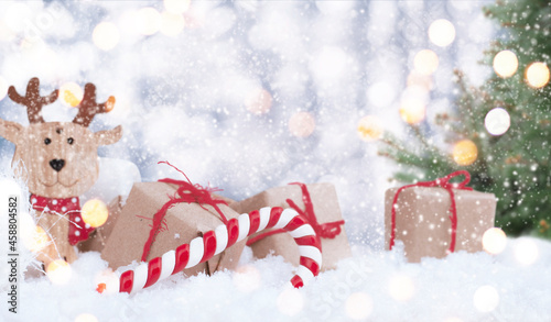 christmas presents with wooden noel, lollipop and christmas tree in the snow with bokeh