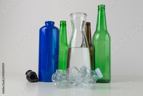 Aluminum water bottle, carafe and glass bottle, with a crumpled plastic bottle next to it. Plastic recycling and use of reusable materials. 