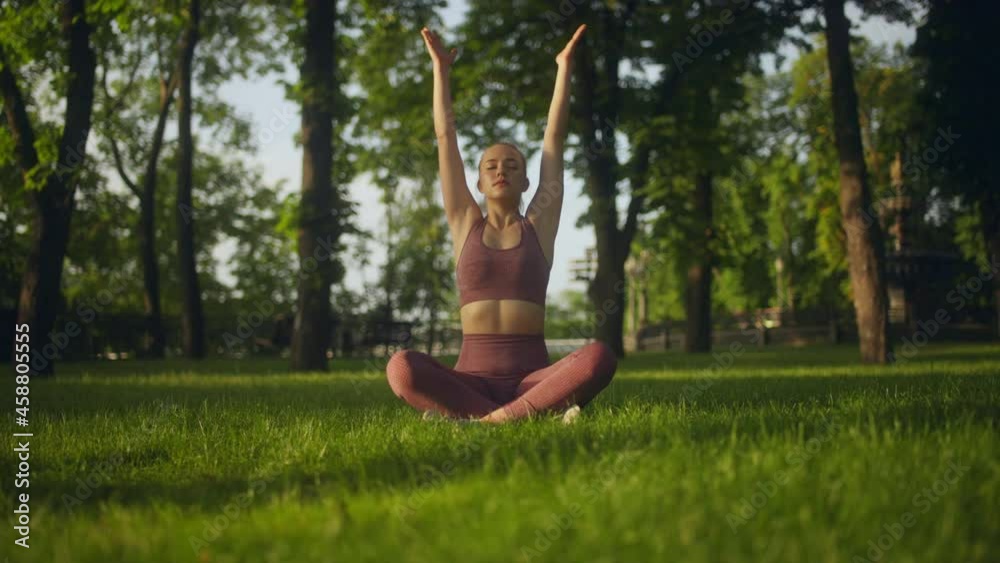 Young woman sitting in lotus pose in park, practicing yoga, meditating outdoors Young woman sitting in lotus pose in park, practicing yoga, meditating outdoors