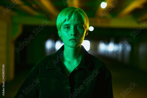 portrait of a girl in a black shirt and with a short haircut who stands in an empty parking lot in a neon green light. High quality photo