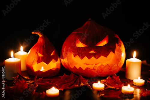 Halloween holiday pumpkin lantern with scary face with candles and dry leaves.