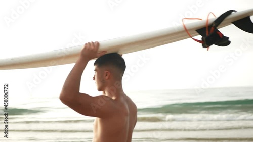 Side view of surfer walking while carrying a surfboard on his head. photo