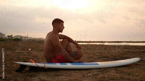 Young brunette surfer waiting with his board on the seashore. photo