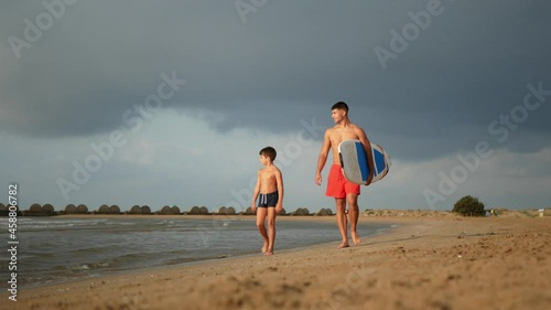 Surfer with his little brother walking on the beach with surfboard. photo