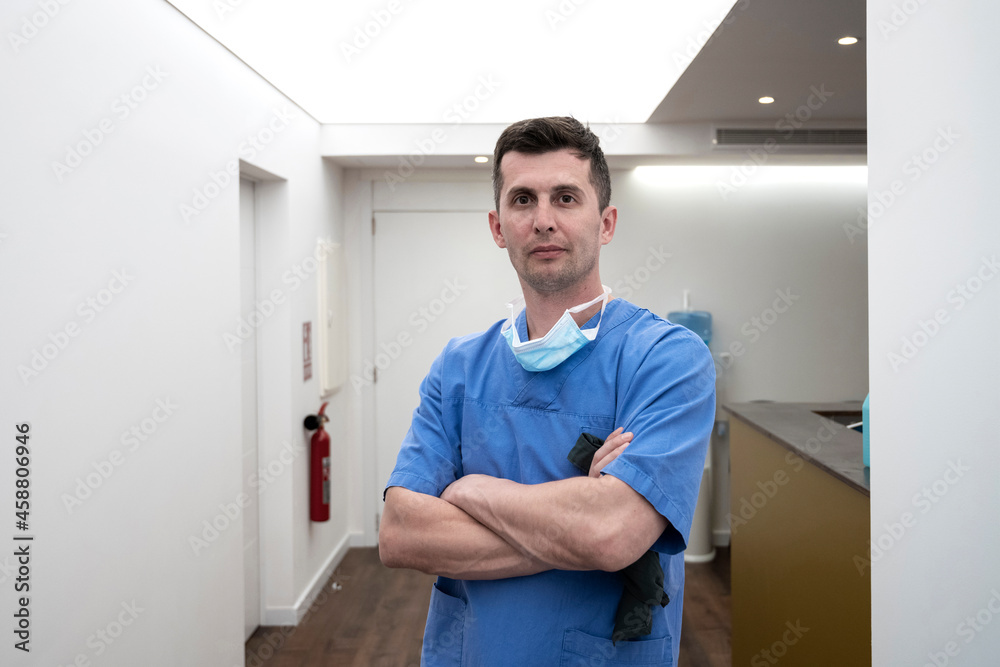 Confident male surgeon standing with arms crossed at hospital