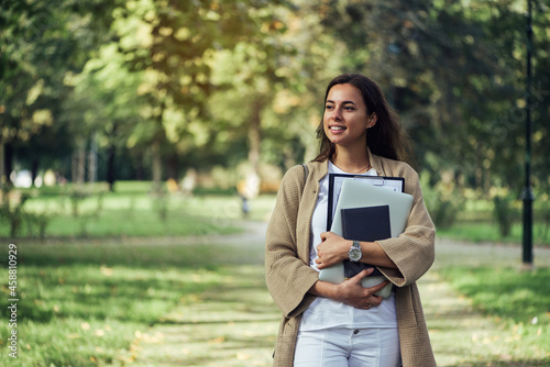 Canvas Print Pretty woman is standing with the folder, notebook and laptop at the summer park background