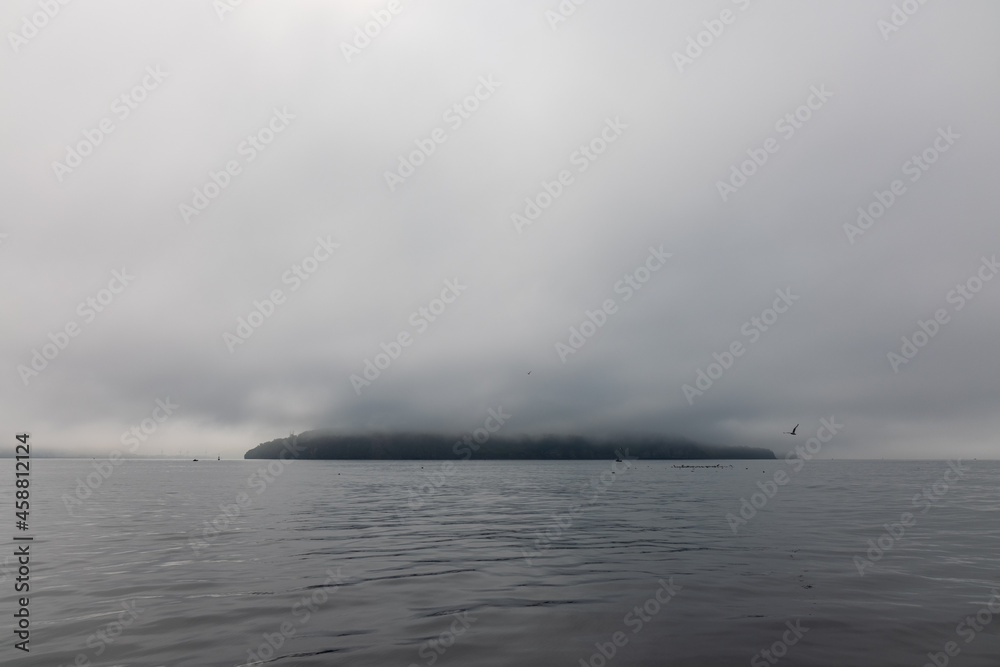 An island in the ocean is hidden by fog and low clouds in the vicinity of Kamchatka.