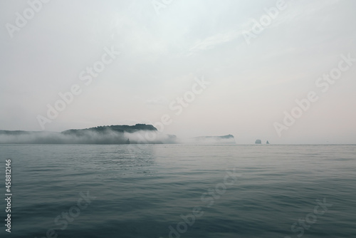 An island in the ocean is hidden by fog and low clouds in the vicinity of Kamchatka. © Ilya