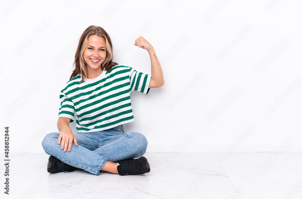 Young Russian girl sitting on the floor isolated on white background doing strong gesture