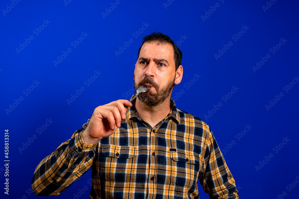 Close-up portrait of attractive skeptic minded guy licking spoon healthy menu nutrition isolated over bright blue color background Close-up portrait of attractive skeptic minded guy licking spoon healthy menu nutrition isolated over bright blue color background