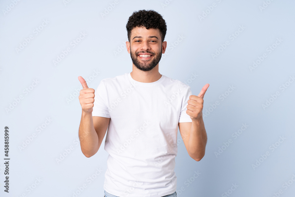 Young Moroccan man isolated on blue background with thumbs up gesture and smiling Young Moroccan man isolated on blue background with thumbs up gesture and smiling