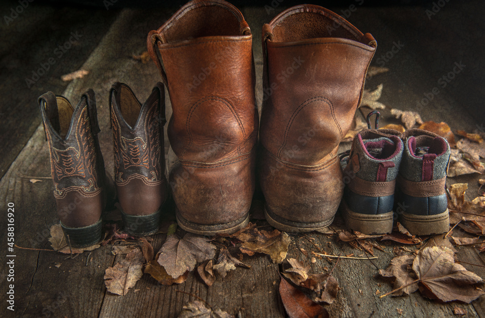 old work boots and childrens boots in fall leaves on wood floor