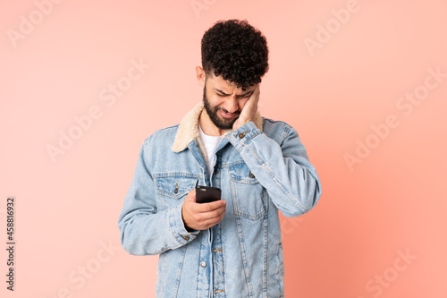 Young Moroccan man using mobile phone isolated on pink background frustrated and covering ears © luismolinero