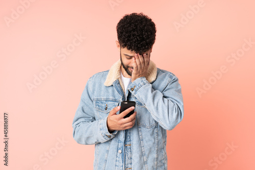 Young Moroccan man using mobile phone isolated on pink background with tired and sick expression © luismolinero