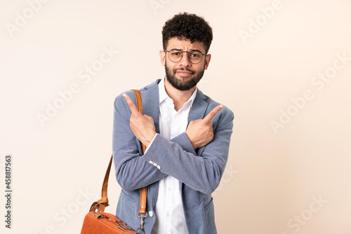 Young business Moroccan man isolated on beige background pointing to the laterals having doubts © luismolinero