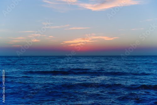 Dark blue water surface background with soft light pink colored cloudy sky. Seascape, no people