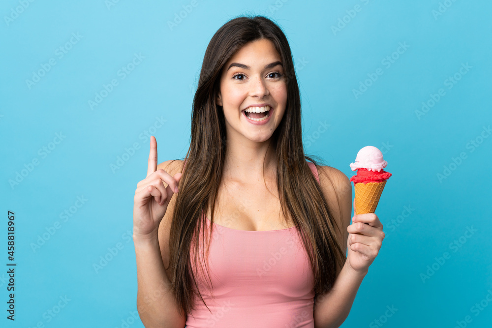 Teenager Brazilian girl holding a cornet ice cream over isolated blue background pointing up a great idea Teenager Brazilian girl holding a cornet ice cream over isolated blue background pointing up a great idea
