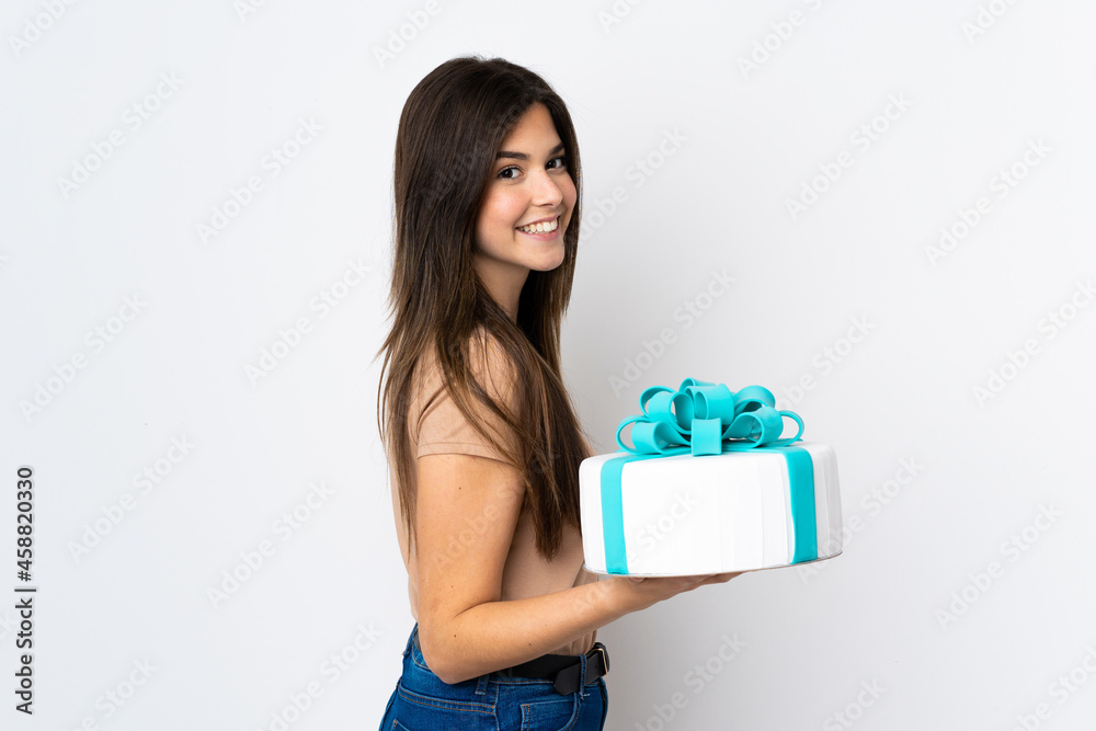 Teenager pastry chef holding a big cake over isolated white background smiling a lot Teenager pastry chef holding a big cake over isolated white background smiling a lot