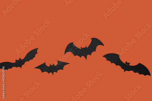 Minimalism style Halloween composition with decorative black bats on bright terracotta background.