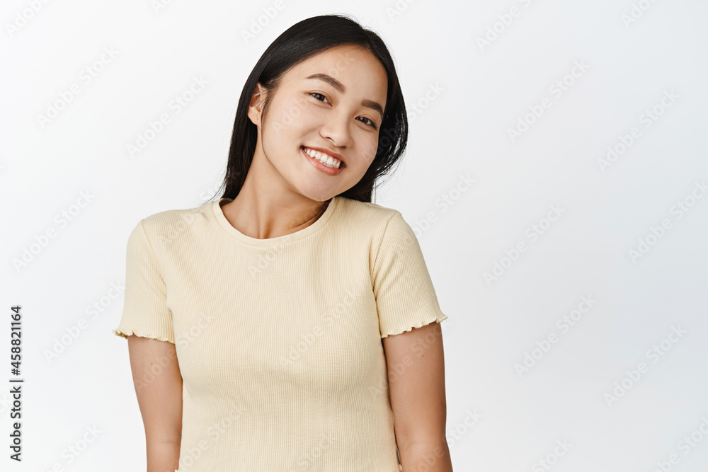 Beautiful smiling asian woman, looking cute and happy at camera, standing in yellow t-shirt over white background Beautiful smiling asian woman, looking cute and happy at camera, standing in yellow t-shirt over white background