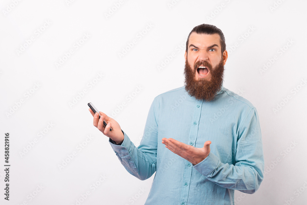 Frustrated bearded man is disappointed in his phone. He is making an unhappy face over white background.