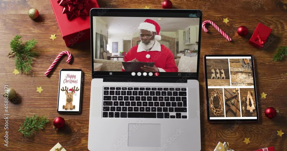 Senior african american santa on video call on laptop, with smartphone, tablet and decorations