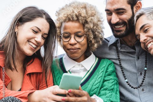 Young diverse group of friends having fun using mobile phone outdoor - Focus on african girl face