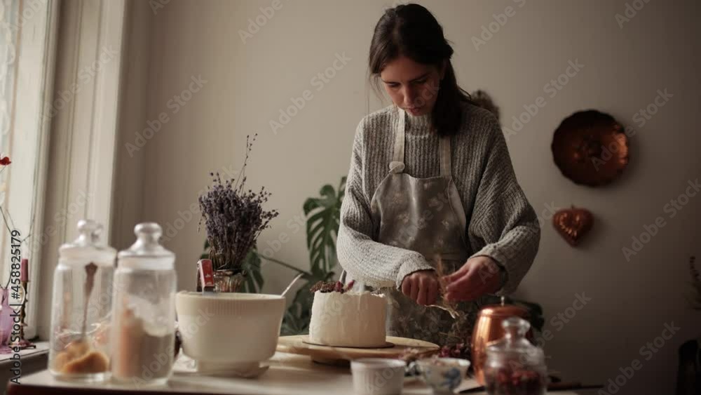 Woman making cake at kitchen workplace. Chef decorates a cake with berries and dried flowers. Unsurpassed pre-holiday atmosphere and home comfort. Homemade bakery concept Woman making cake at kitchen workplace. Chef decorates a cake with berries and dried flowers. Unsurpassed pre-holiday atmosphere and home comfort. Homemade bakery concept