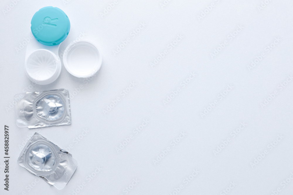 A container for lenses and two sealed lenses lie on the side on a white background with space for text. top view, flat lay, copy space, isolate A container for lenses and two sealed lenses lie on the side on a white background with space for text. top view, flat lay, copy space, isolate
